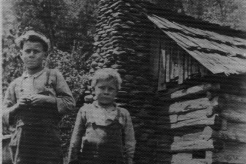 Black and white historic photo of two boys standing in front of log cabin in Great Smoky Mountains National Park at Tremont.