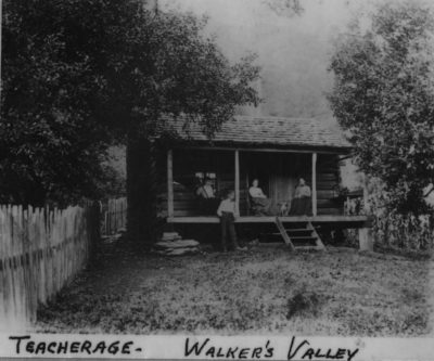 Historical photo of Walker Valley Teacherage, a log cabin with a surrounding fence.