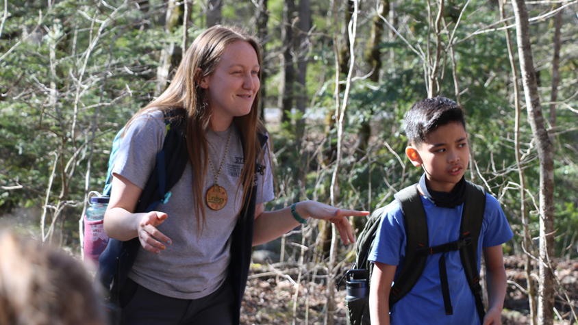 Lindsey describes an activity to a group of students in the woods at Tremont.